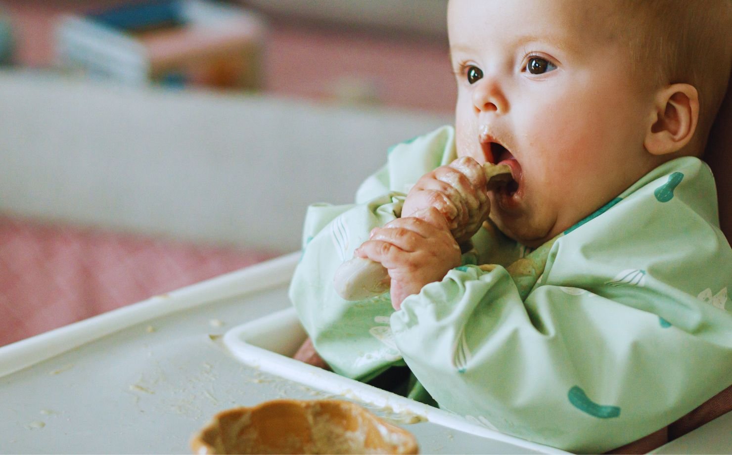 Bebé feliz en una silla alta probando su primera comida en la alimentación complementaria.